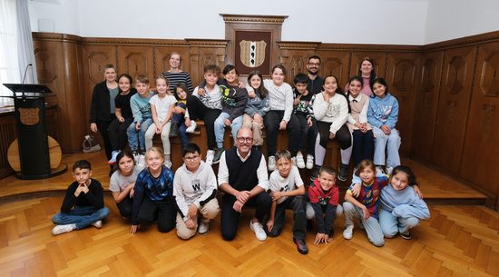 Das Bild zeigt die Klasse 3a der Volksschule Schendlingen, die gemeinsam mit ihrem Lehrpersonal und Bürgermeister Michael Ritsch im Stadtvertretungszimmer des Bregenzer Rathauses ein Erinnerungsfoto machen.