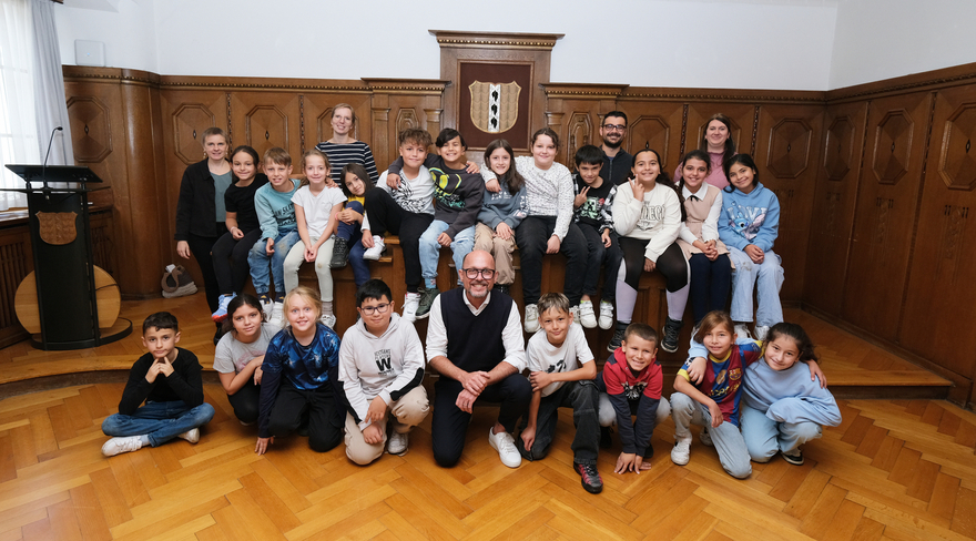 Das Bild zeigt die Klasse 3a der Volksschule Schendlingen, die gemeinsam mit ihrem Lehrpersonal und Bürgermeister Michael Ritsch im Stadtvertretungszimmer des Bregenzer Rathauses ein Erinnerungsfoto machen.