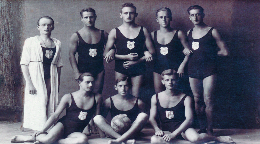 Dieses Schwarz-Weiß-Foto zeigt acht junge Männer. Alle tragen Sportanzüge, einer davon noch einen Umhang darüber.