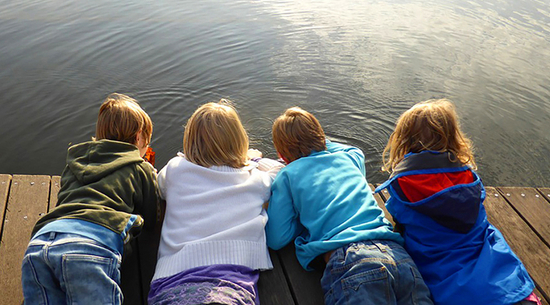 Diese Abbildung zeigt vier Kinder, welche auf einem Steg am Wasser liegen.