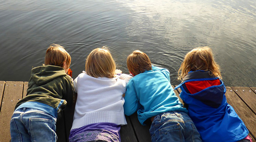 Diese Abbildung zeigt vier Kinder, welche auf einem Steg am Wasser liegen.