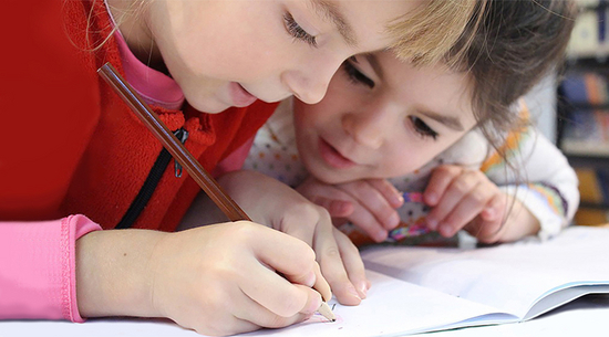 Diese Abbildung zeigt zwei junge Mädchen, welche etwas in ein Heft schreiben.