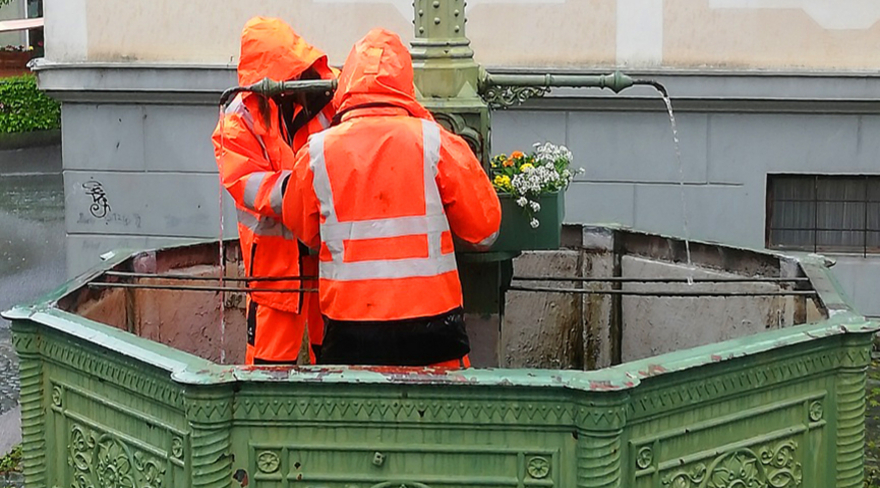 Hier sind zwei Mitarbeiter der Stadtgärntnerei abgebildet, welche den städtischen Brunnen bepflanzen.