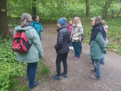 Auf dem Foto sieht man Karin Müller Vögel mit sechs Frauen, die ihr zuhören, im Wald bei einem Waldspaziergang. 