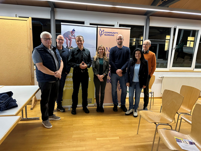 Das Bild zeigt den Vortragenden Heinz Fuchsig mit Mitarbeiter:innen der Stadt Bregenz und Vertreter:innen der Politik in einem Saal stehen. Hinter ihnen sind Roll-Ups zu erkennen.