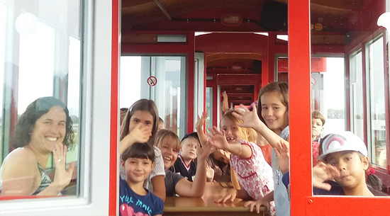 Hier wurden einige Kinder und eine Begleitperson im Rheinbähnle fotografiert. Alle winken in die Kamera.