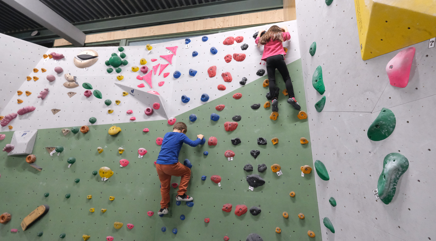 Das Bild zeigt zwei Kinder von hinten, die eine Kletterwand hinaufklettern. 