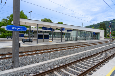 Auf dem Foto sieht man bei Tag einen Bahnsteig mit zwei Gleisen und der Tafel "Bregenz" in Blau davor. 