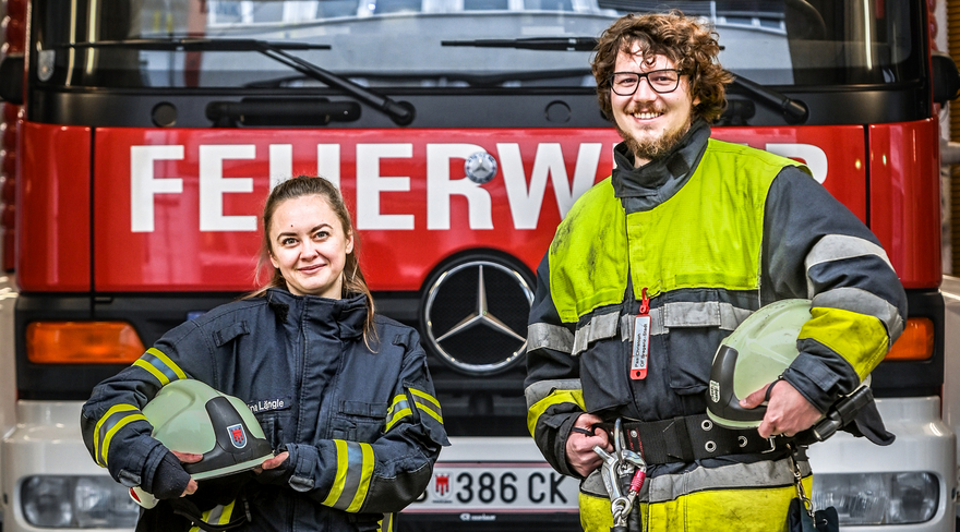 Das Bild zeigt zwei Feuerwehrleute vor dem Löschfahrzeug. 