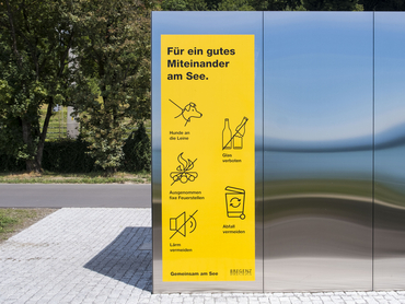 Auf dem Bild ist ein Hinweisplakat in gelb zu sehen mit den Regeln zum Verhalten am Seeufer.
