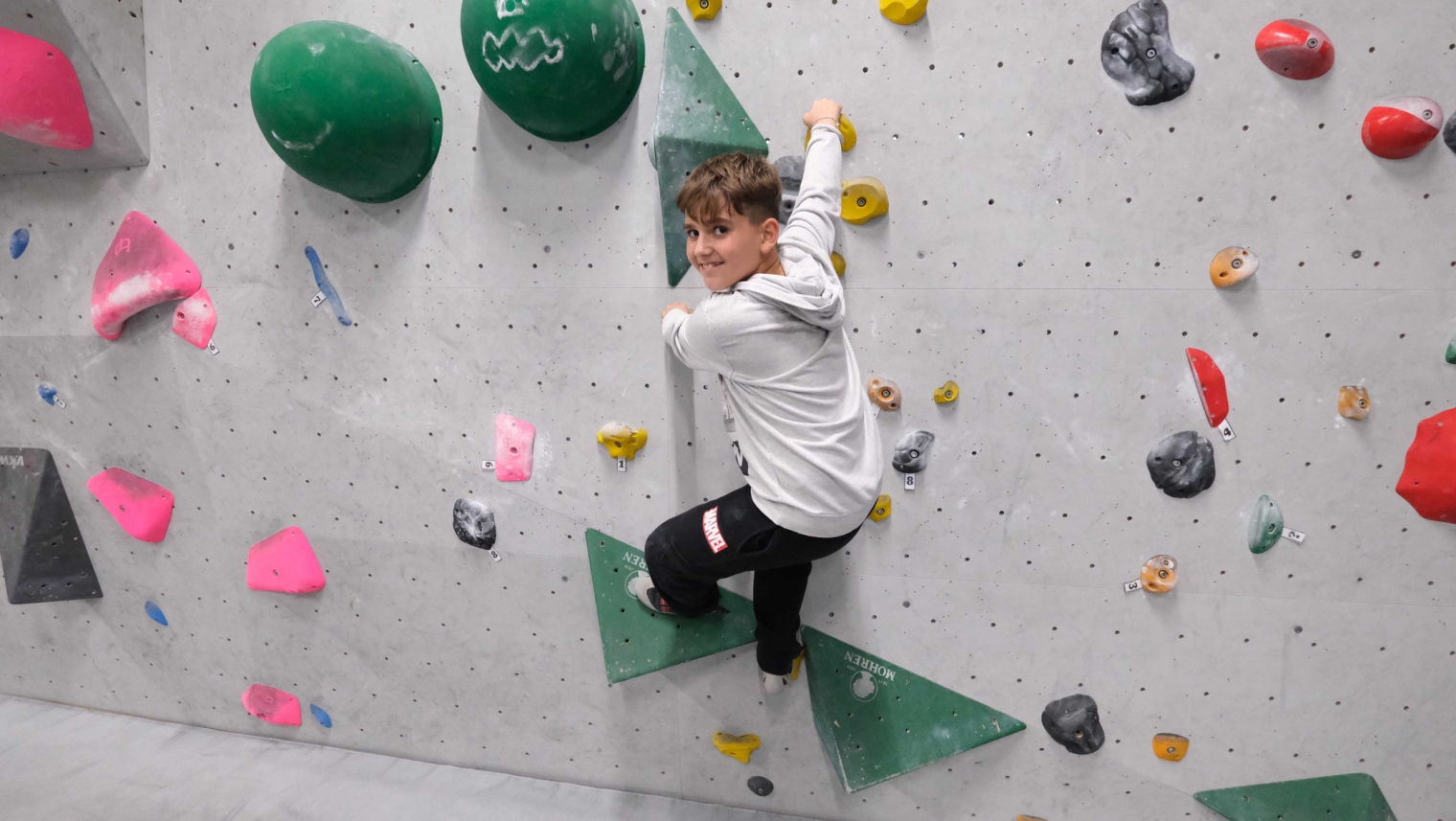 Auf dem Bild ist ein Schüler während der Schülerbetreuung zu sehen, der in der Boulderhalle an einer Wand hängt.