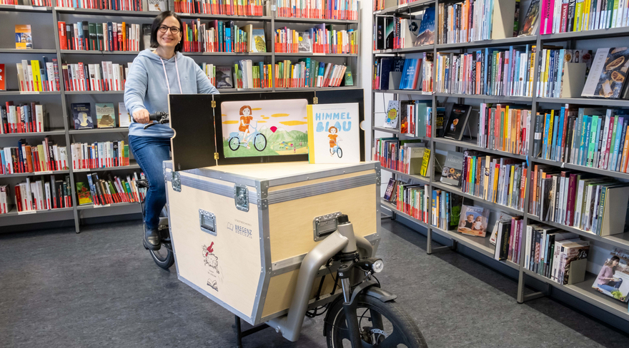 Auf dem Bild ist eine Mitarbeiterin der Stadtbücherei Bregenz zu sehen, die auf einem "Tag der Inklusion"-Fahrrad sitzt. 