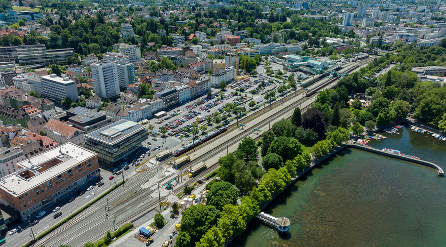 Das Bild zeigt eine Luftaufnahme des innerstädtischen Entwicklungsgebietes mit dem großen Seestadt-Parkplatz, der Landesstraße, dem Bahnhof etc.