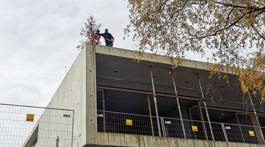 Diese Abbildung zeigt zwei Bürger, welche auf einer Baustelle einen Tannenbaum anbringen.