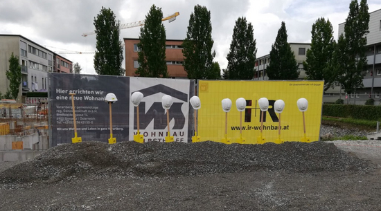 Diese Abbildung zeigt eine Baustelle in Bregenz. Schaufeln wurden in den Boden gesteckt und Schutzhelme oben drauf gesetzt.