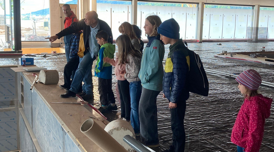 Das Bild zeigt eine Baustellenbegehung des neuen Seebades in Bregenz mit Kindern. Projektleiter Bernd Raica zeigt den Kinderreportern ein neues Innenbecken auf der Baustelle.