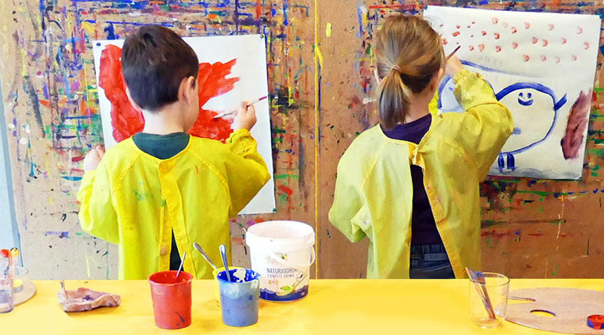 Diese Abbildung zeigt zwei Kinder beim malen. Sie tragen beide einen gelben Mantel.