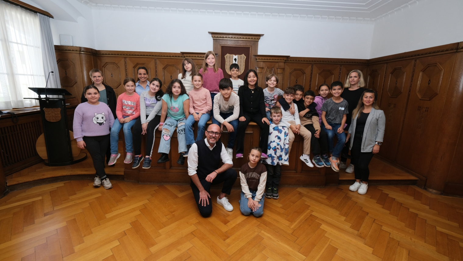 Das Bild zeigt die Klasse 3a der Volksschule Schendlingen, die gemeinsam mit ihrem Lehrpersonal und Bürgermeister Michael Ritsch im Stadtvertretungszimmer des Bregenzer Rathauses ein Erinnerungsfoto machen.