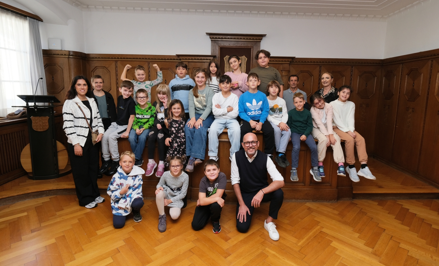 Das Bild zeigt die Klasse 3a der Volksschule Schendlingen, die gemeinsam mit ihrem Lehrpersonal und Bürgermeister Michael Ritsch im Stadtvertretungszimmer des Bregenzer Rathauses ein Erinnerungsfoto machen.