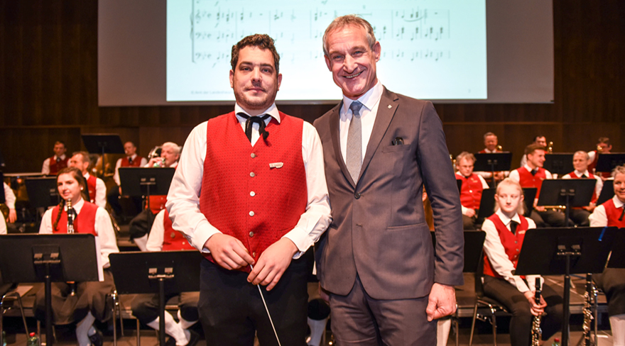 Diese Abbildung zeigt Markus Linhart mit dem Kapellmeister der Stadtmusik Bregenz. Im Hintergrund sind die Musiker der Stadtmusik Bregenz zu sehen.