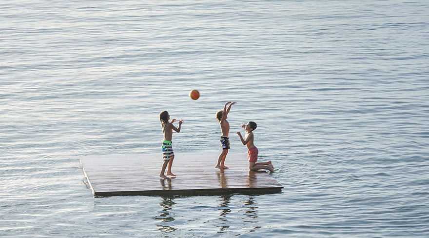 Diese Abbildung zeigt Kinder, welche auf einem Floß im See mit einem Ball spielen.