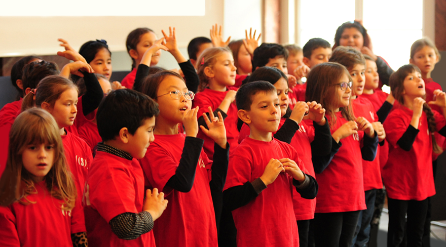 Diese Abbildung zeigt Kinder, welche alle ein rotes T-Shirt tragen und in einem Chor singen.